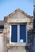 Photographie d'une lucarne au fronton triangulaire sur fond de toit en ardoise.