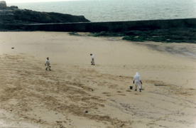 Photographie de trois hommes en combinaison blanche sur une plage.