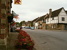 Large rue de village, bordée de maisons anciennes, dont une à colombages