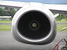 A zoomed-in view of the front of an engine nacelle: The fan blades of the engine are in the middle of the image. They are surrounded by the engine nacelle, which is seemingly circular on the top half, and flattened on the bottom half.