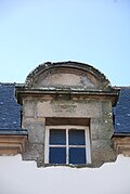 Photographie d'une lucarne arrondie, sur fond de toit en ardoise.