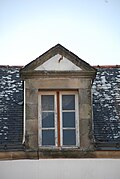 Photographie d'une lucarne au fronton triangulaire, sur fond de toit en ardoise.