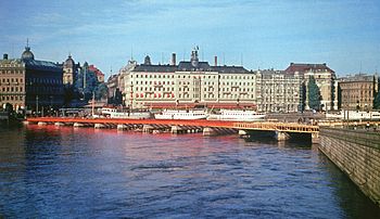 Strömbron under uppförande 1946 och sedd från samma plats år 2010. Bron grundlades provisoriskt på träpålar, som sticker upp över vattenytan, vilket framgår på bilden från 1946. I bakgrunden syns Grand Hôtel innan takvåningen påfördes.