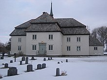 Foto einer weißen Holzkirche. Im Vordergrund ein von Schnee bedeckter Friedhof.