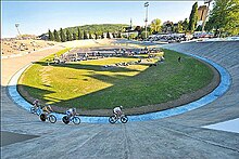 Photographie d'un vélodrome en plein air avec quatre coureurs en piste.